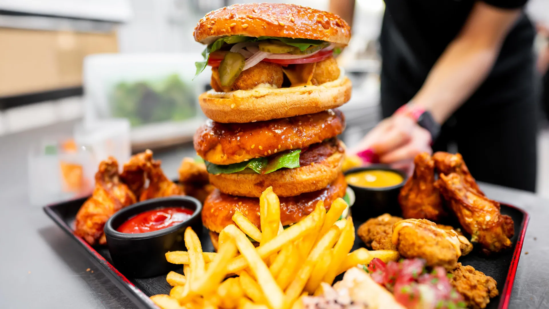 A towering triple-decker burger with chicken wings and French fries, representing ultra-processed foods.